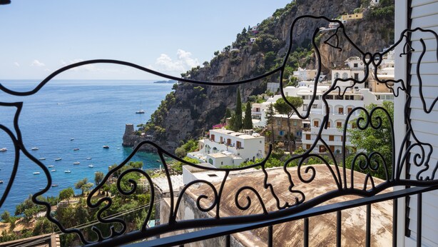 A balcony with a view of a coastal town, featuring buildings, a cliff, and the sea. - Casa Lauro (Positano)