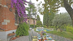 Un área de comedor al aire libre con una mesa preparada para una comida, rodeada de follaje y una piscina al fondo.