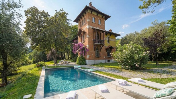 Una piscina con sillones de descanso, un jardín y un edificio grande con una torre.