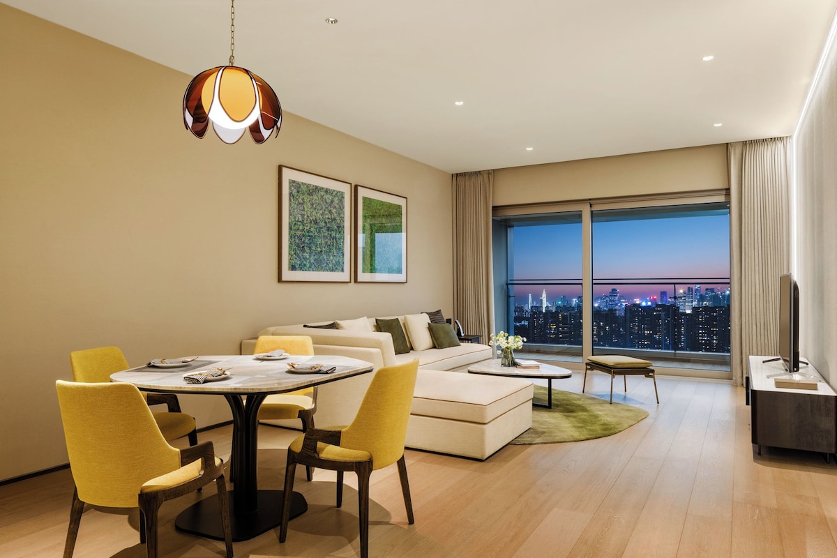 A modern living room with a dining area, a sofa set, a coffee table, and a large window with a city view.