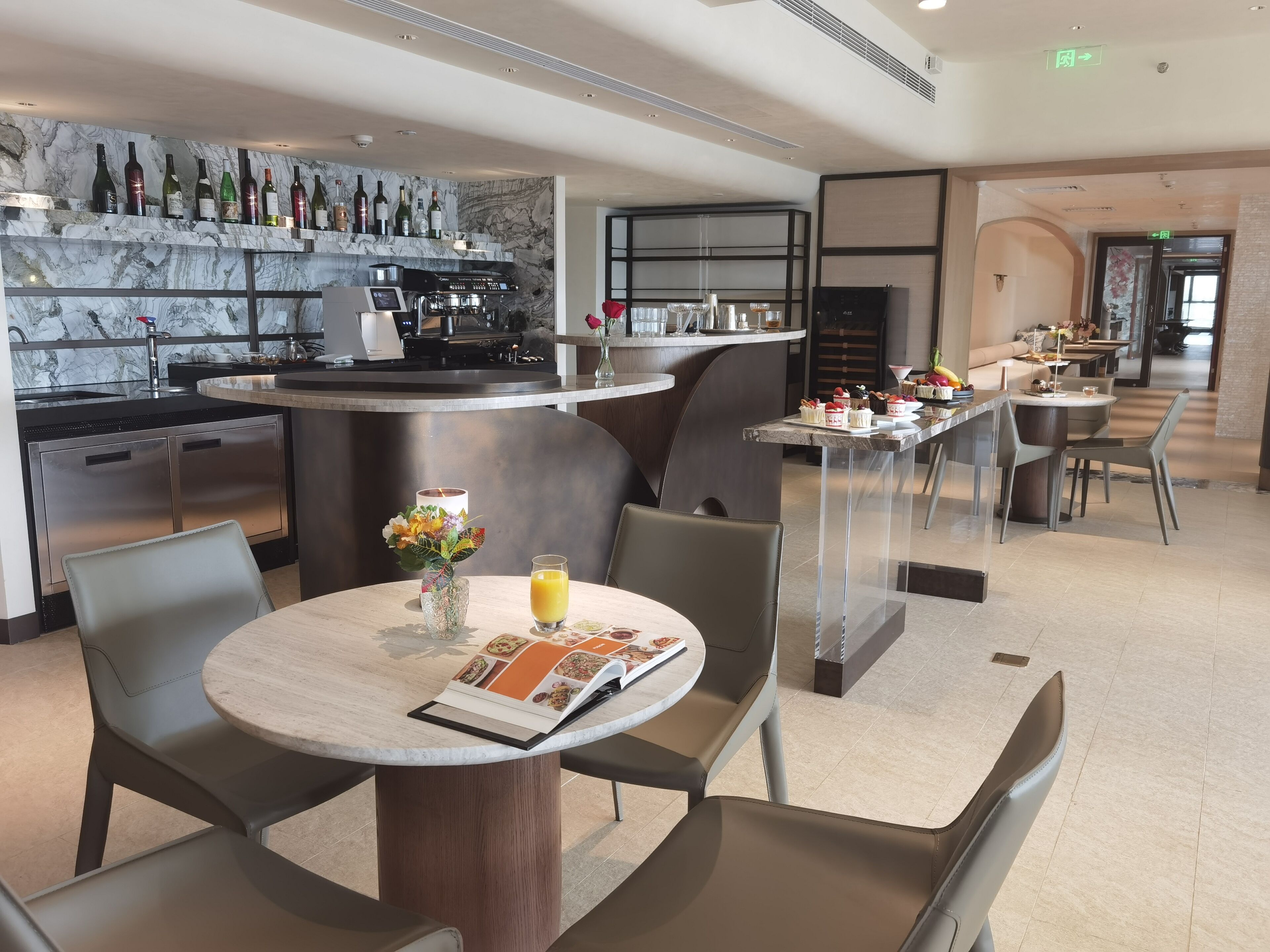 A modern hotel lobby with a marble reception desk, a bar area with wine bottles, and a dining area with a menu.