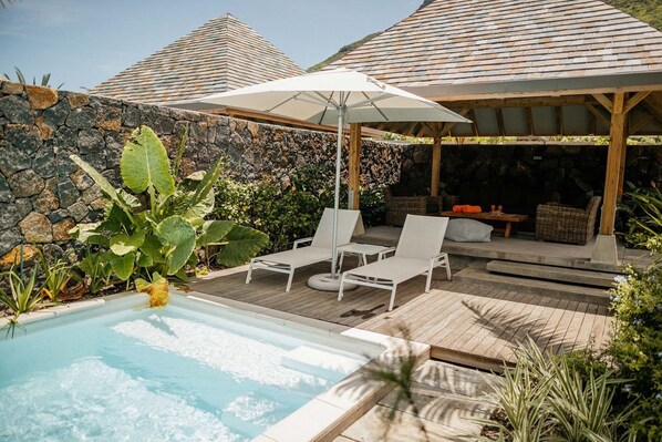 Relax by the serene pool surrounded by lush greenery and a wooden pergola.