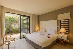 Relax in a serene space with a spacious bed, bedside table, and chair, plus a balcony with a view of lush greenery.