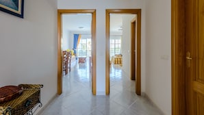 Un couloir avec une porte en bois sur la droite et un miroir qui reflète une pièce avec un lit et une fenêtre.