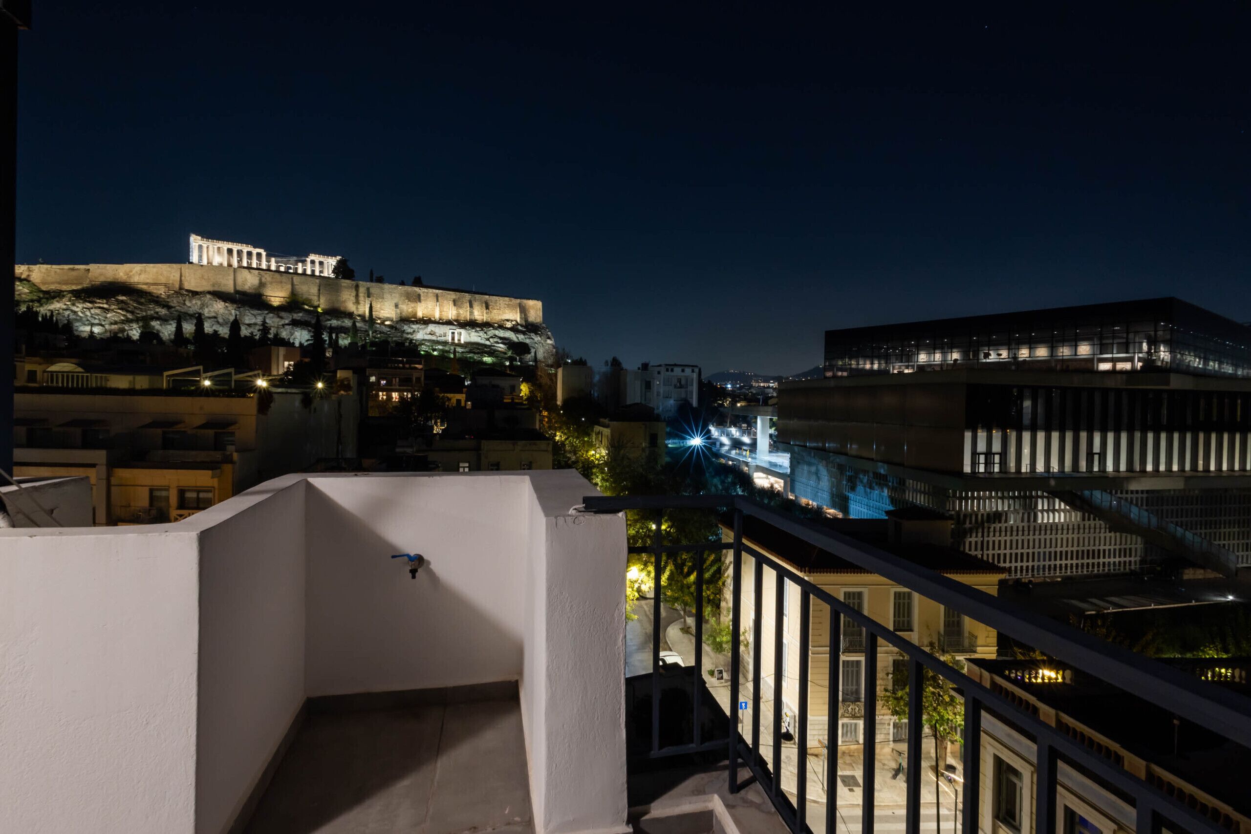 Vue nocturne d'un bâtiment dont les enseignes sont illuminées, avec un balcon et des constructions urbaines environnantes.