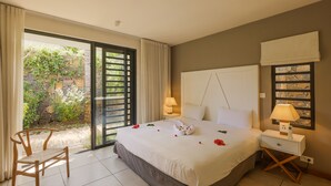 Hotelkamer met een bed, nachtkastje, stoel en uitzicht op een tuin door een schuifdeur.