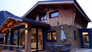 Una cabaña de madera con terraza, ventanas amplias y zona de comedor.