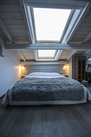Une chambre dotée d’une lucarne, de poutres apparentes, d’un lit recouvert d’un plaid en fourrure et d’un éclairage intégré.