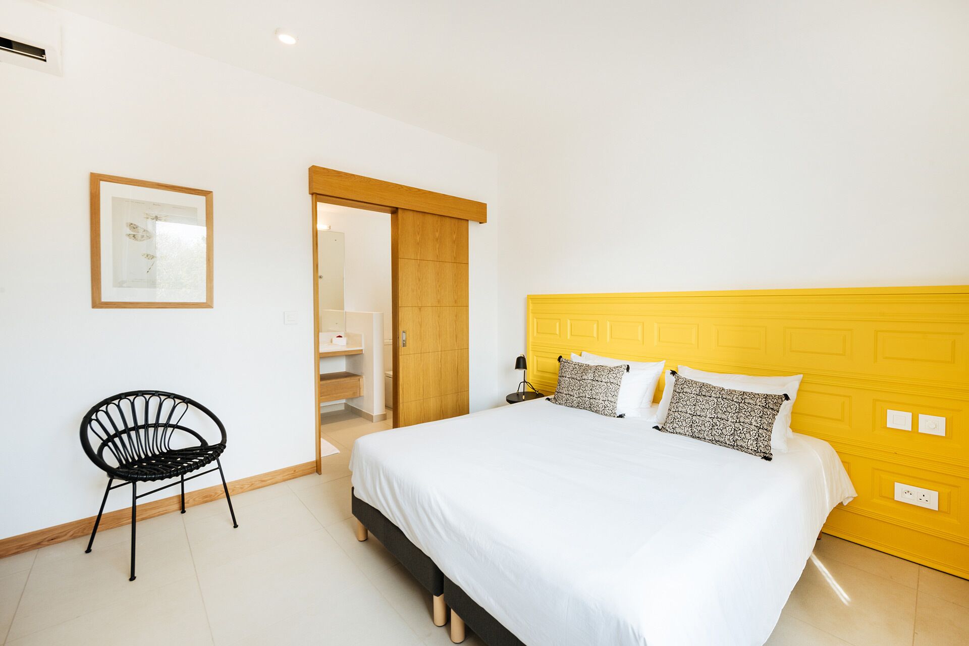 A bedroom with a bed, a chair, a wooden door, and a framed picture on the wall.