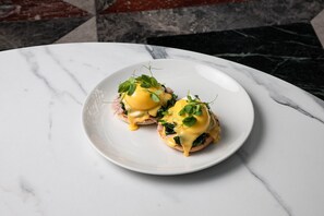 Een wit bord met twee eggs benedict sandwiches op een marmeren tafel.