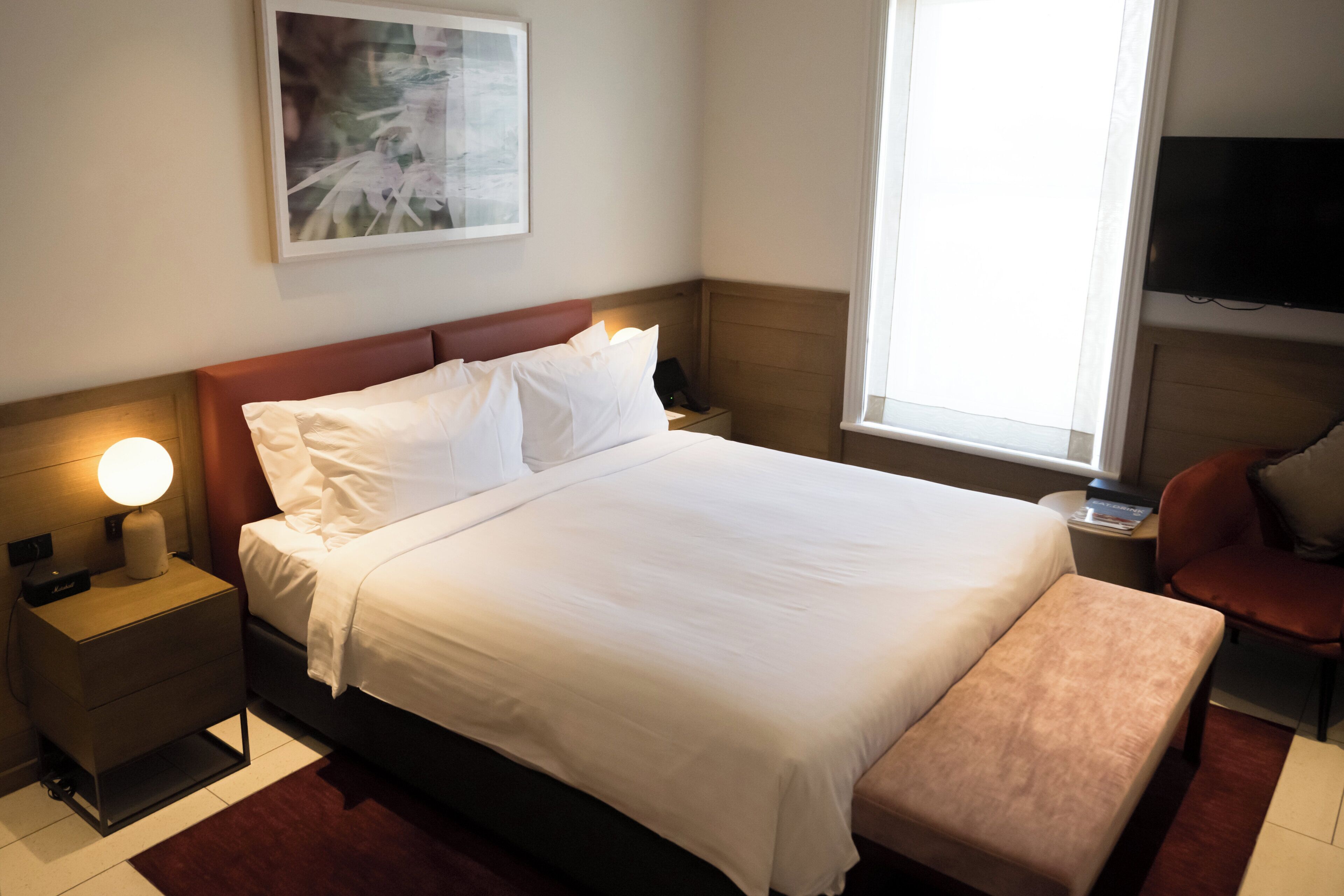 A neatly made bed with white linens, a bedside lamp, and a small bedside table.