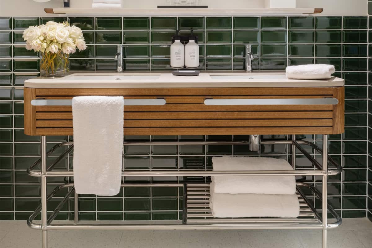 Een moderne badkamer met een houten wastafelmeubel, twee spiegels, een groene betegelde achterwand en een handdoekhouder.