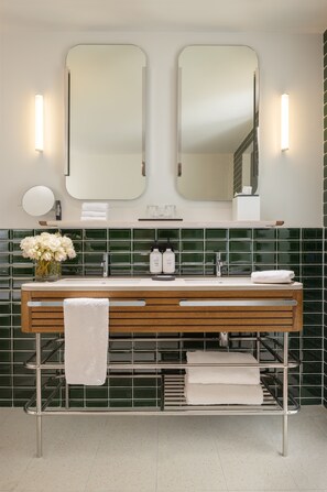 Een moderne badkamer met een houten wastafelmeubel, twee spiegels, een groene betegelde achterwand en een handdoekhouder.
