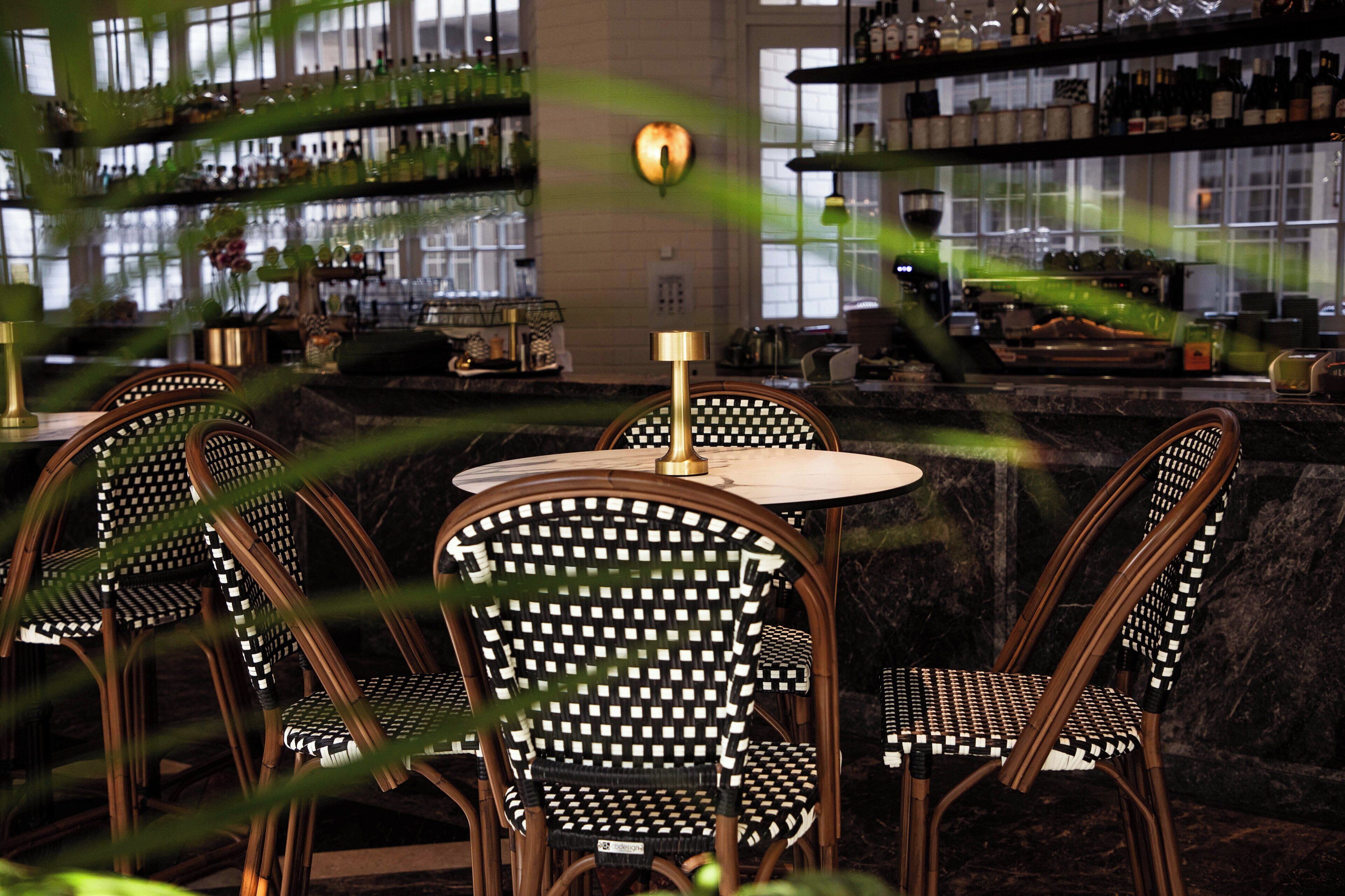 A bar area with wicker chairs, a round table, and shelves of bottles.