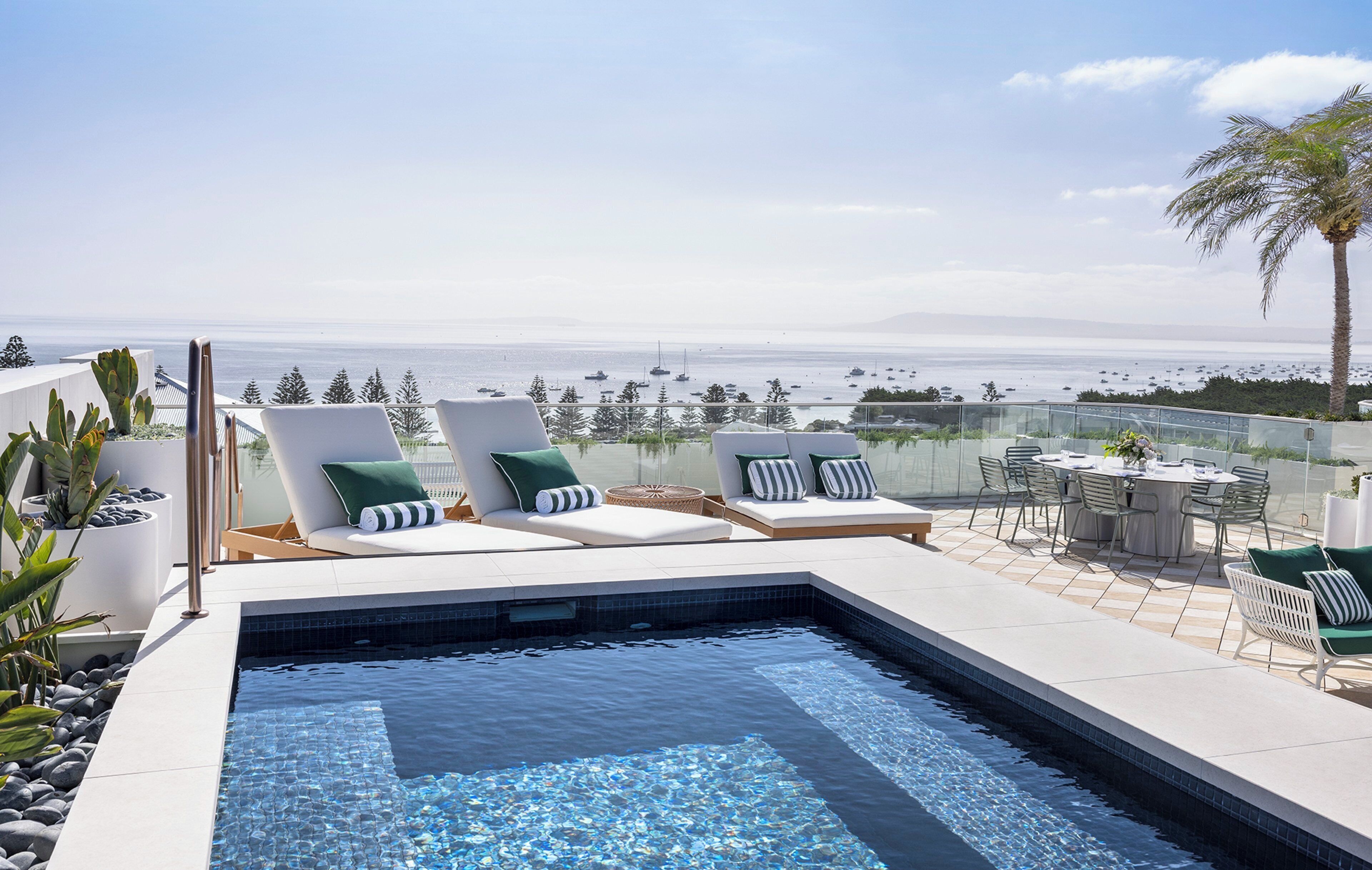 A rooftop pool with lounge chairs and a dining area overlooking a marina.