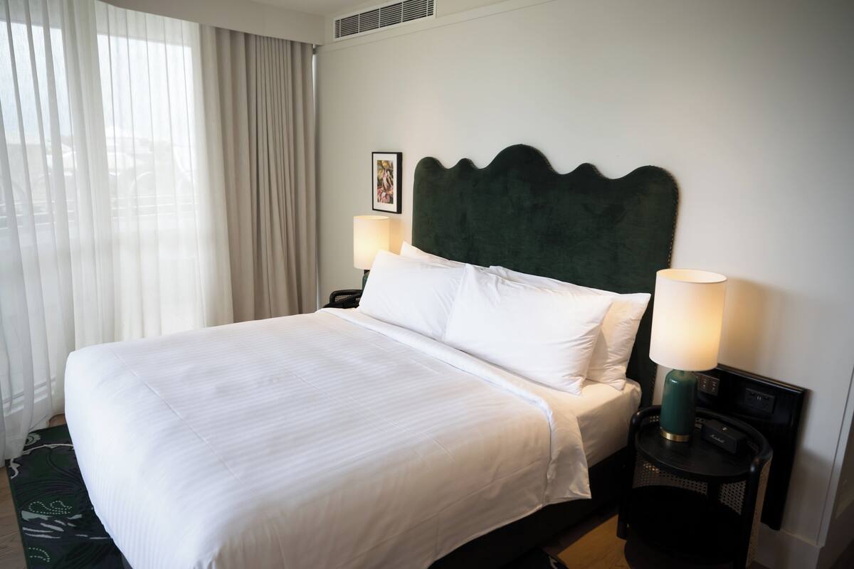 Een net opgemaakt bed met witte lakens, twee bedlampjes en een ingelijst schilderij aan de muur.