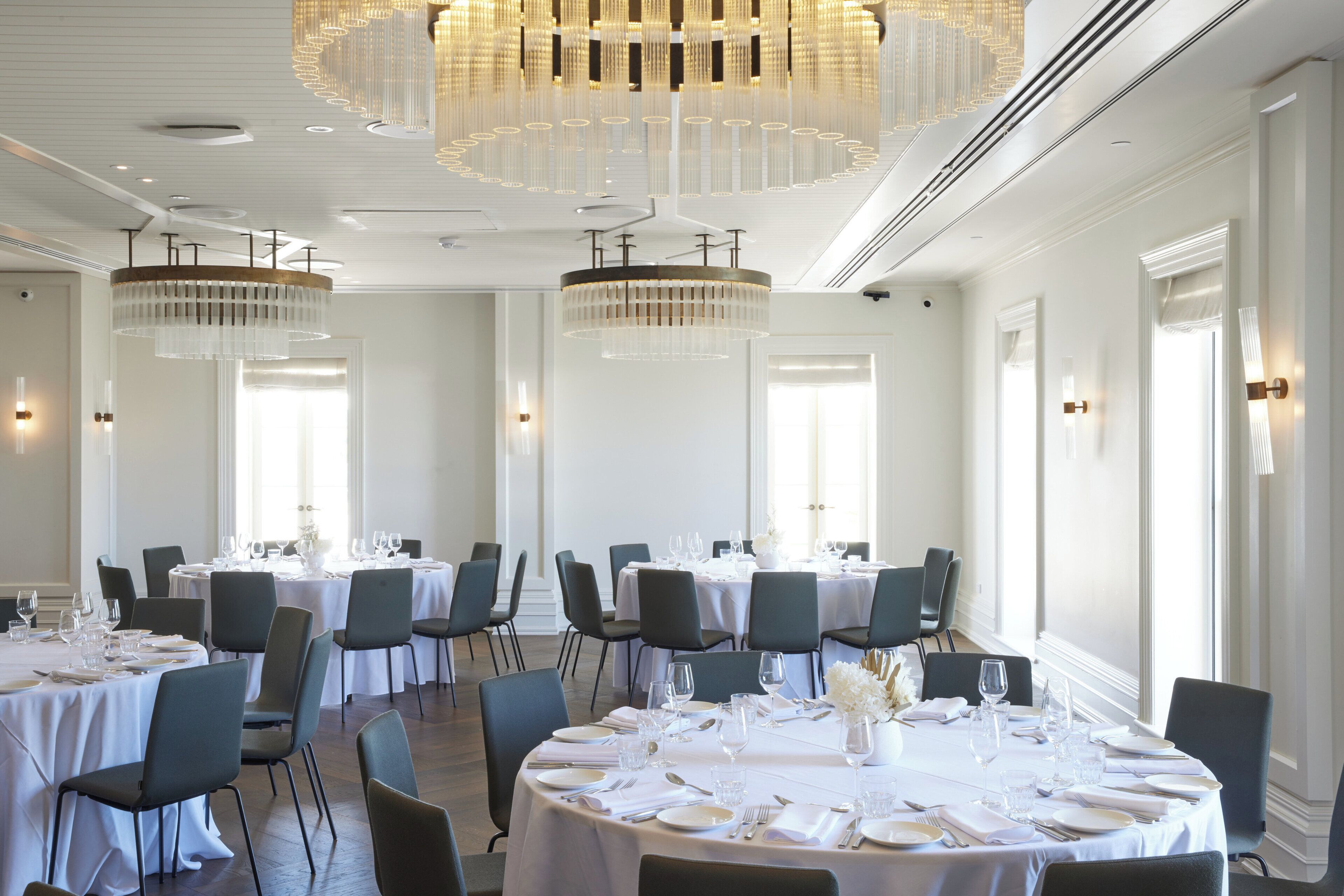 A hotel dining area with round tables, chairs, and chandeliers.