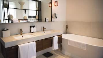 A modern bathroom with two sinks, a large mirror, and a bathtub. There are towels hanging on the side of the bathtub and a black scale on the floor.
