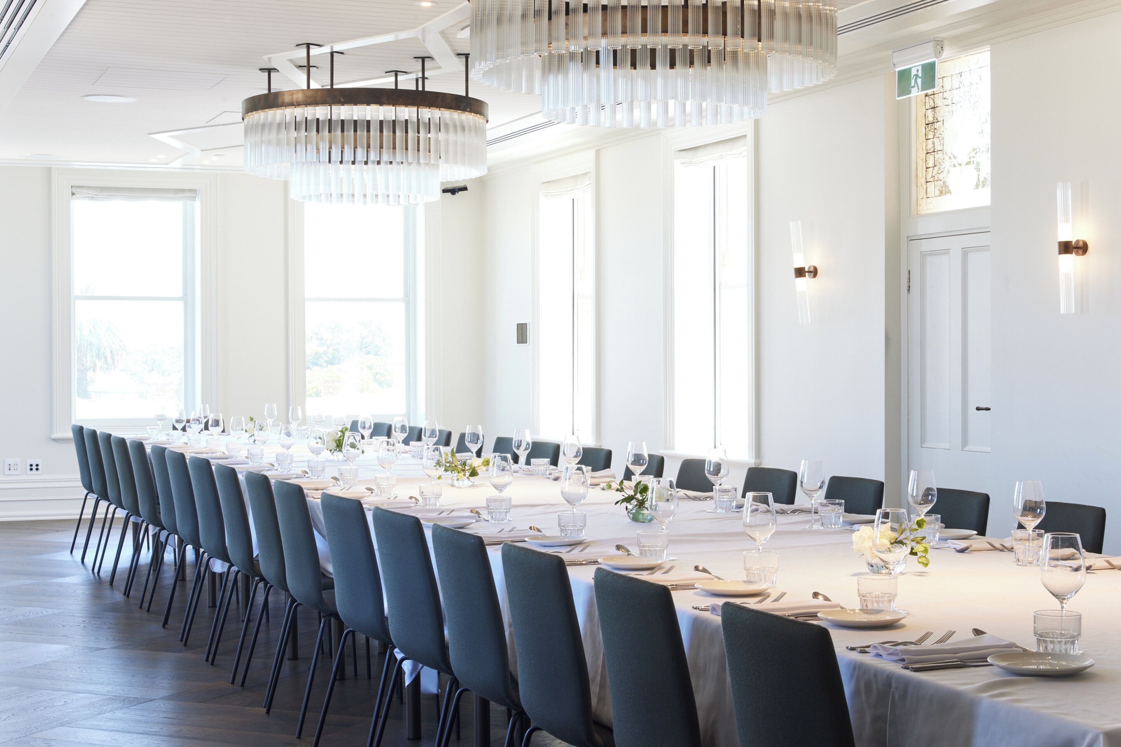 A long dining table set for a formal event with chairs, glassware, and a chandelier.