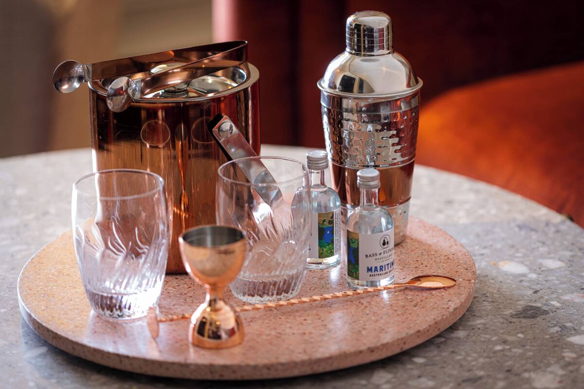 Cocktailspullen met een koperen shaker, een martini glas, een maatbeker en een fles Martini op een ronde tafel.