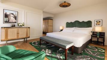 A neatly arranged bedroom with a bed, bedside tables, a green chair, a wooden cabinet, and a decorative rug.