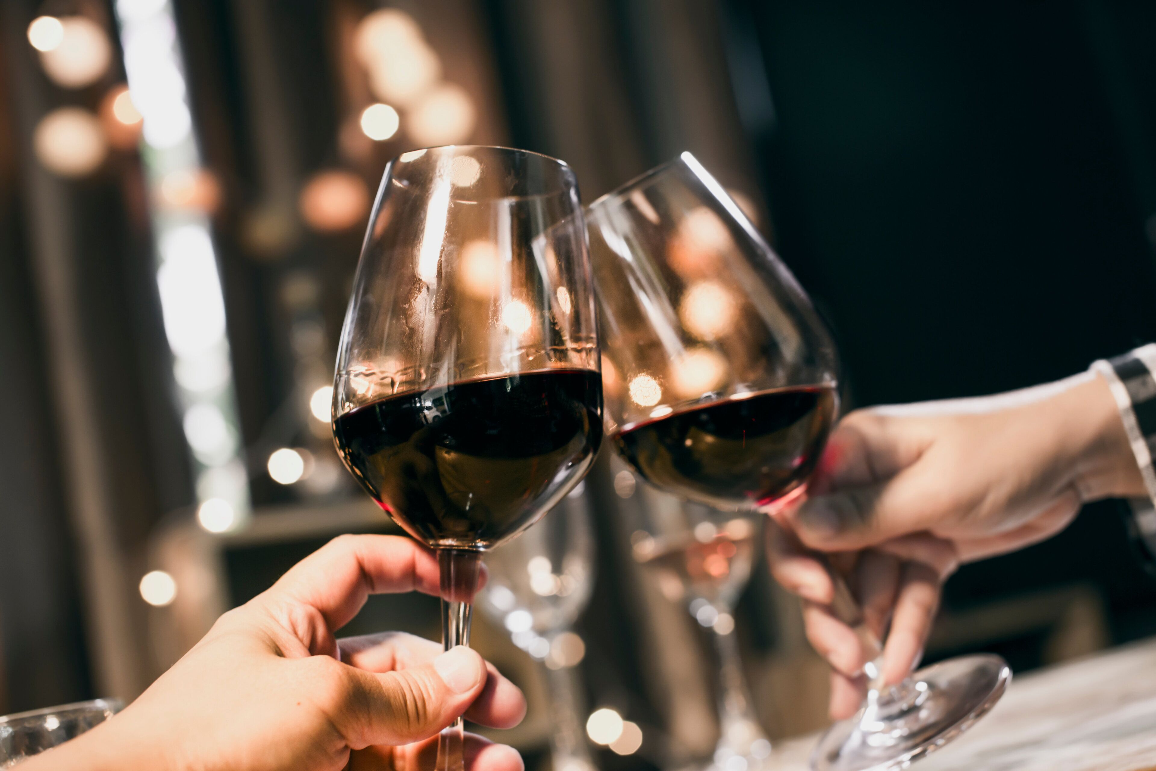 Two hands holding wine glasses filled with red wine, suggesting a social or dining setting.