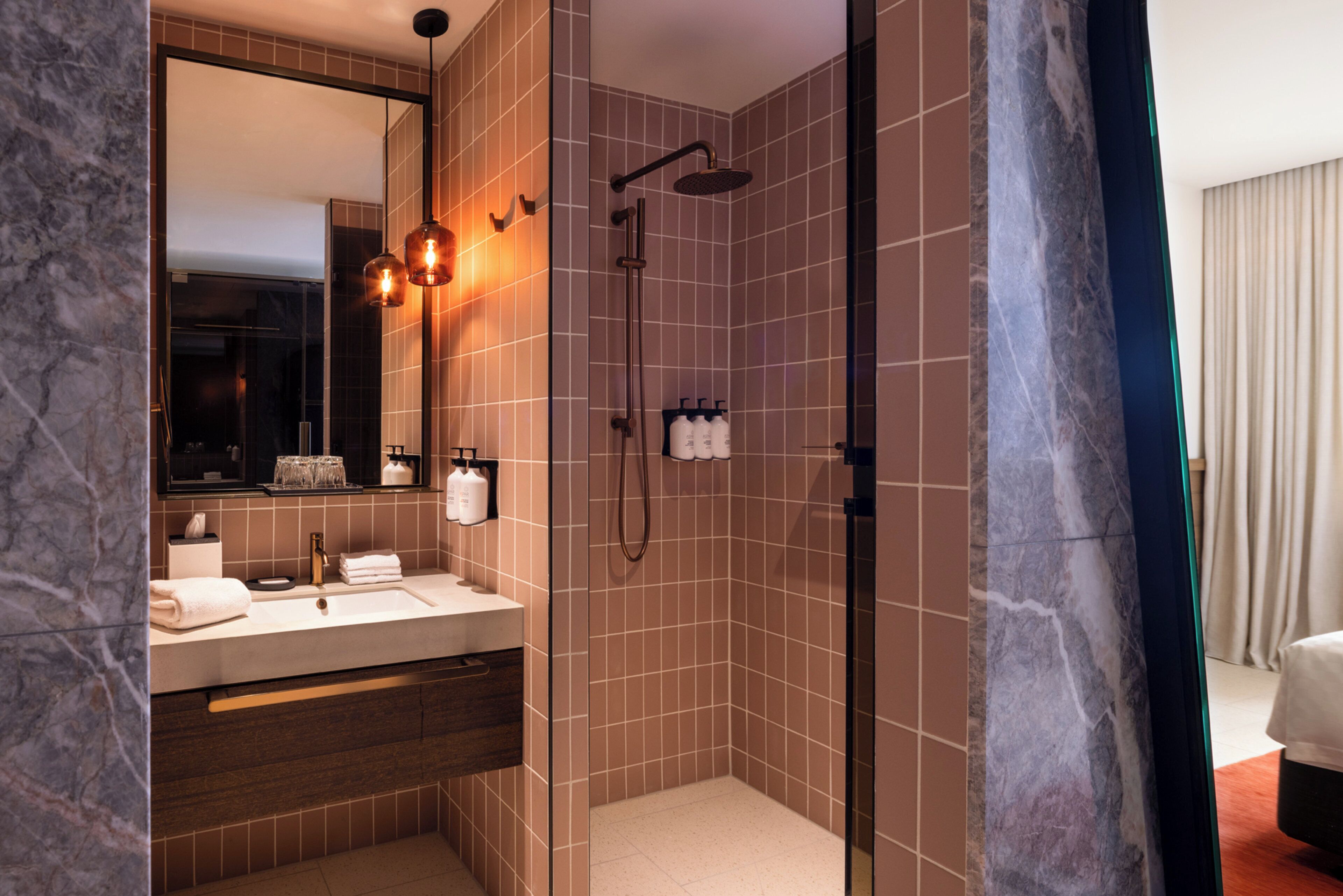 Un baño moderno con lavamanos de mármol, ducha con mampara de vidrio y un espejo grande.