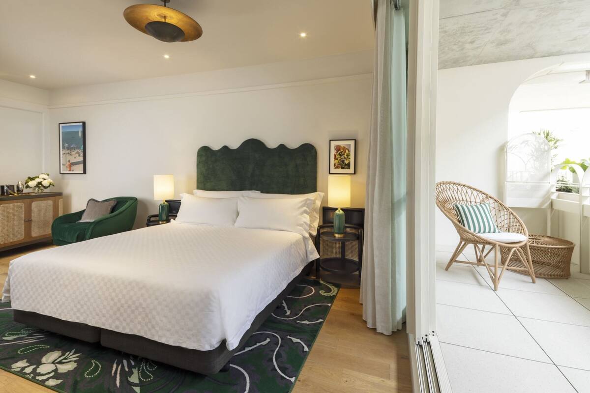Een moderne hotelkamer met een groot bed, een groene stoel, een rieten stoel en uitzicht op het strand.