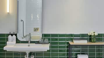 A bathroom with a white sink, a mirror, green tiled walls, and a small table with a vase of flowers.