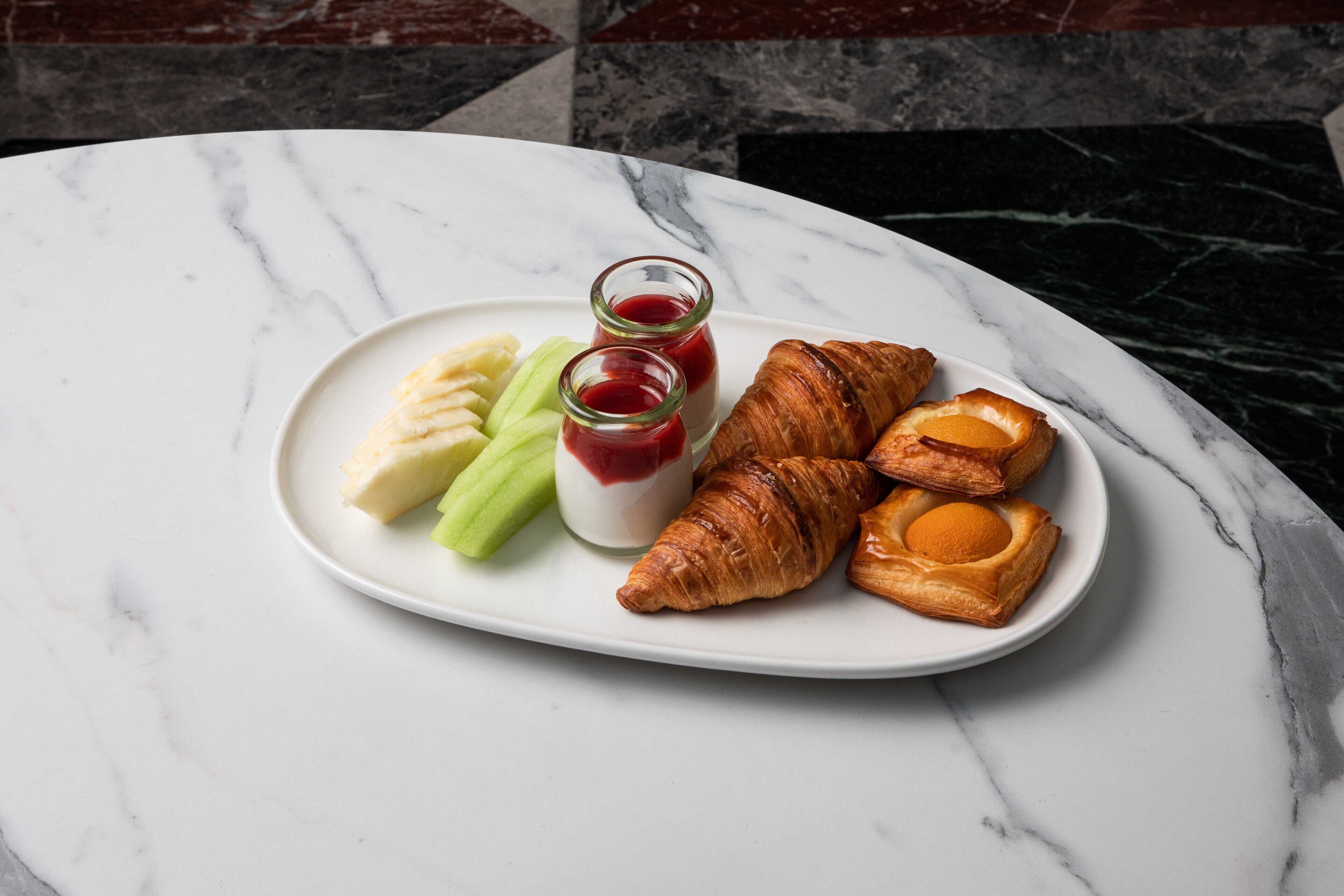 Un plato con croissants, yogur y fruta sobre una mesa de mármol.