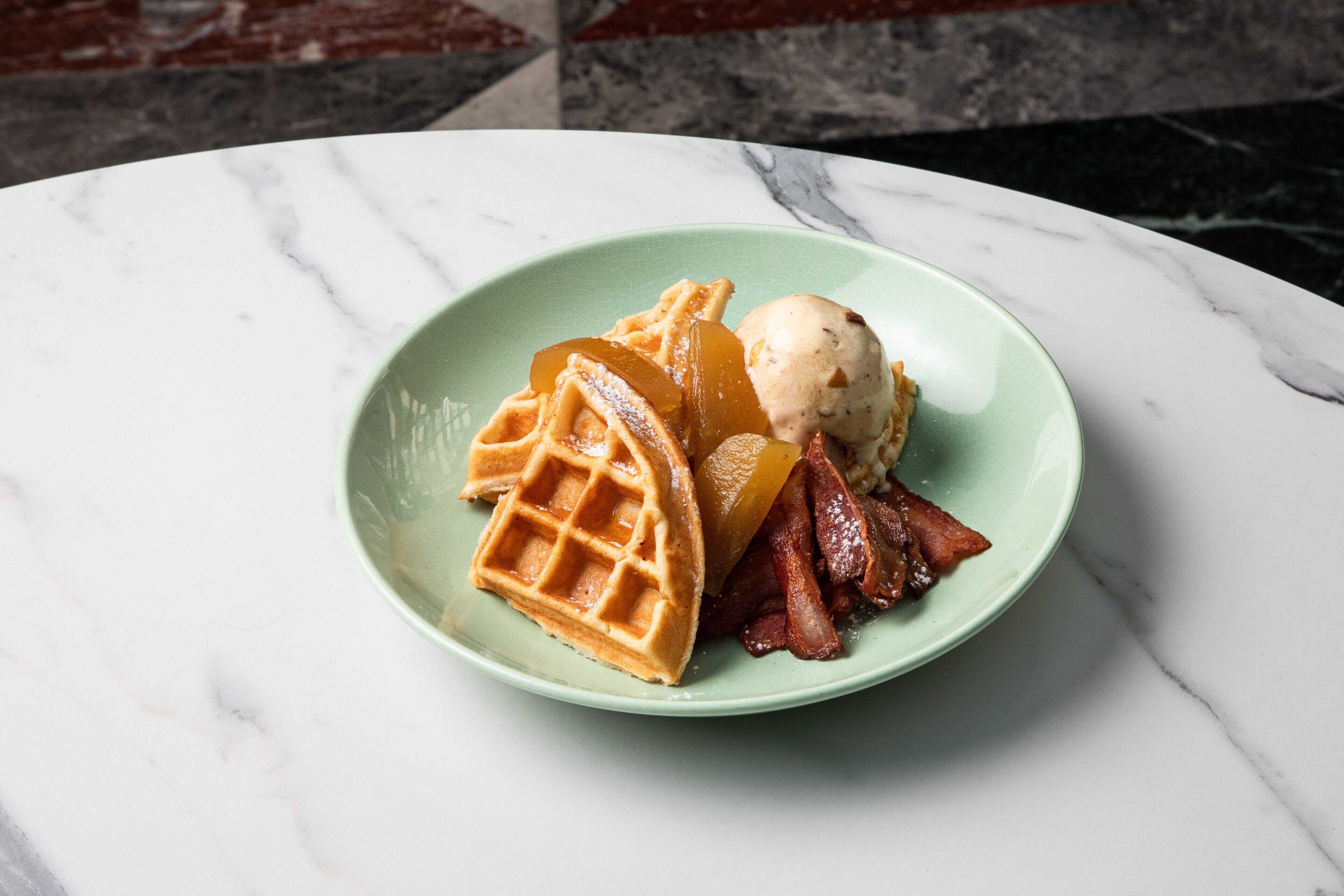 Un piatto con waffle, pancetta e una pallina di gelato su una superficie in marmo.