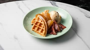 Un piatto con waffle, pancetta e una pallina di gelato su una superficie in marmo.