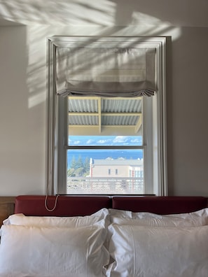 Een kamer met een bed, een raam met uitzicht op gebouwen en een blauwe lucht, plus een gordijn.