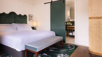 A neatly made bed with a bench, a green door, and a bathroom visible through an open door.