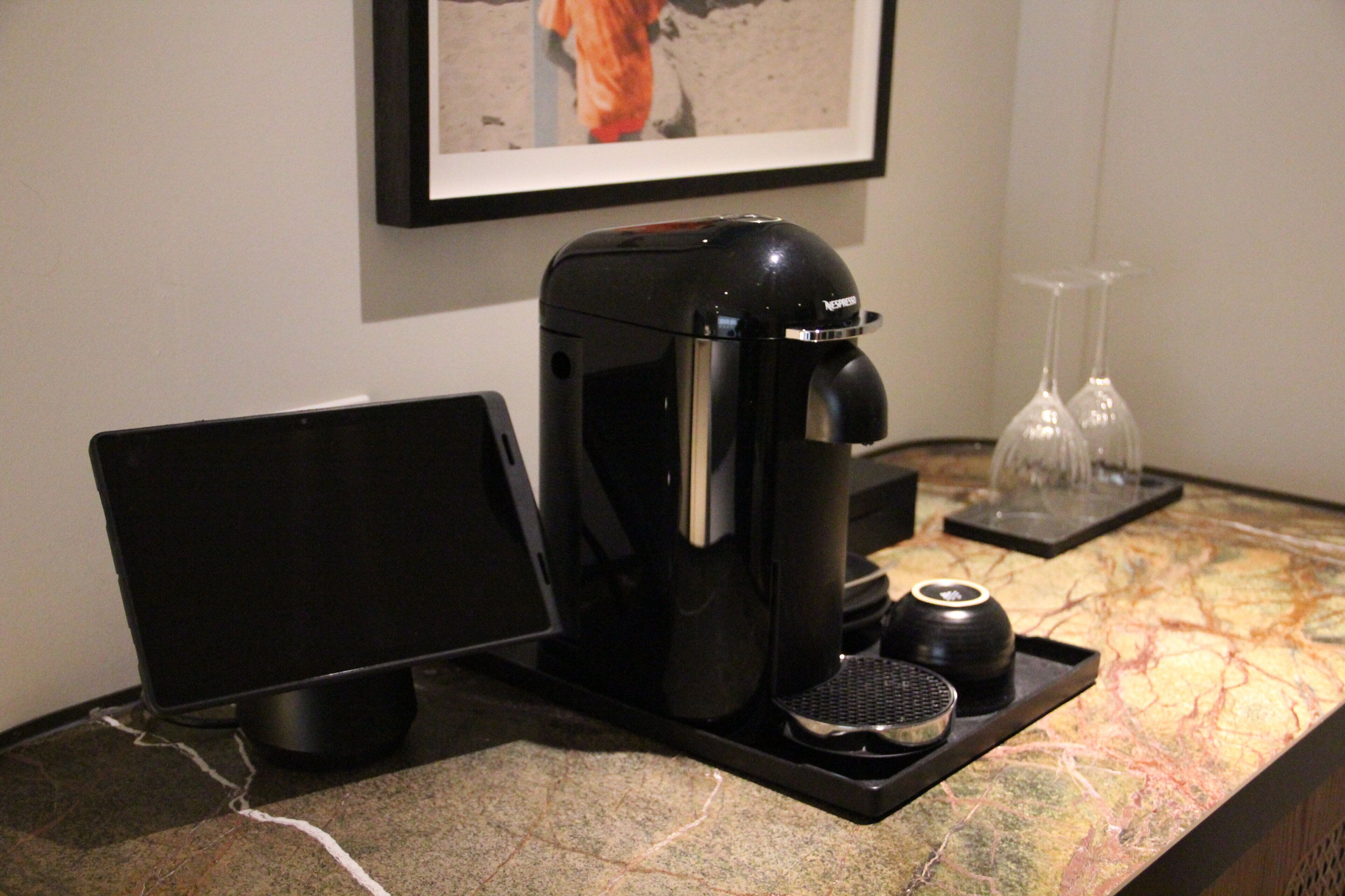 A coffee maker, a tablet, and two glasses on a countertop.