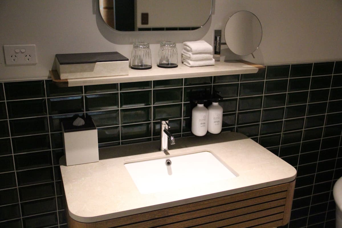Een badkamer met een wit wastafel, een spiegel erboven en een plank met toiletartikelen.