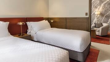 Een hotelkamer met twee bedden, een nachtkastje met lamp, een stoel en een marmeren muur.