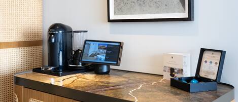 A hotel reception desk with a coffee machine, a digital screen displaying a hotel directory, and a framed welcome sign.
