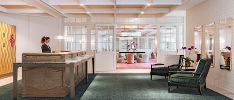 A reception area with a wooden reception desk, a green carpet, and a seating area with a green upholstered chair and a table.
