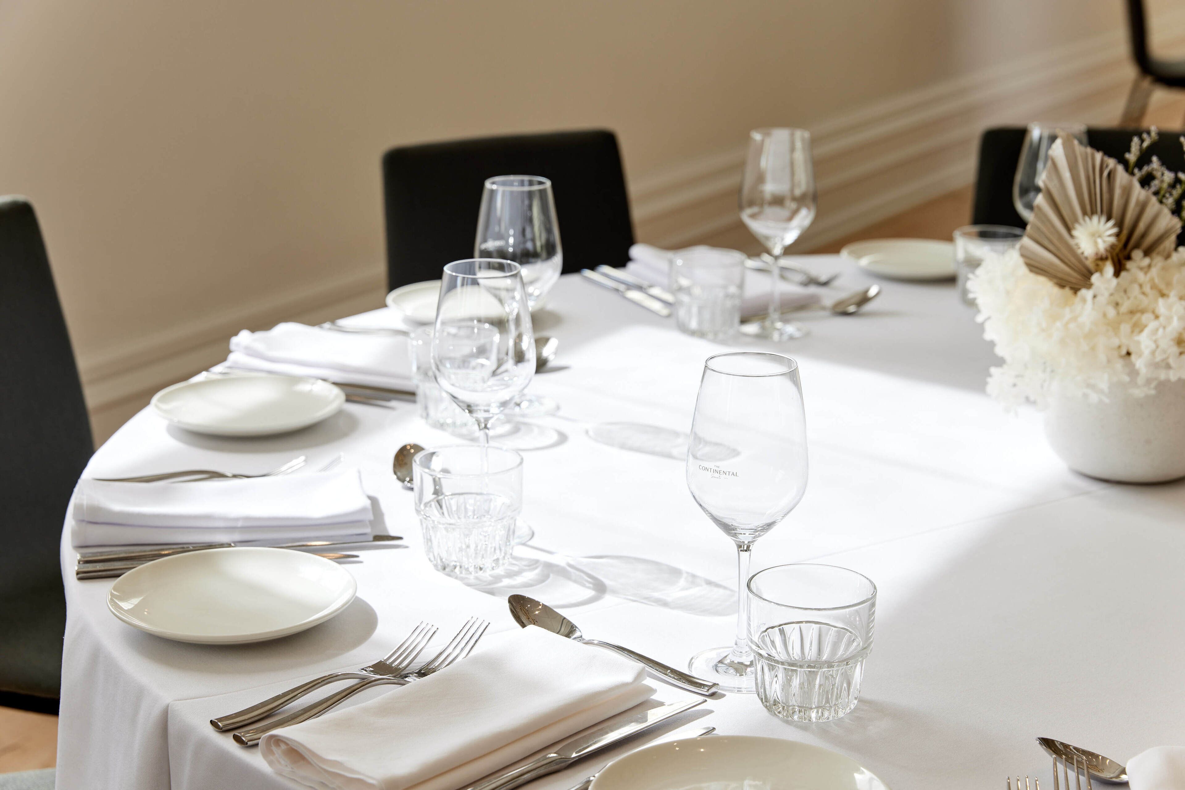 Une table à manger élégamment dressée, avec une nappe blanche, des assiettes, des couverts et des verres transparents.