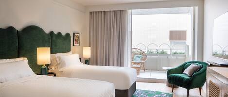 A hotel room with two beds, a green armchair, a window with curtains, and a balcony with a wicker chair.