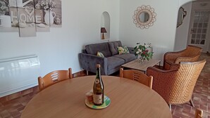 En matplats med ett runt träbord, sex stolar, en vinflaska och ett litet glas. I bakgrunden syns en grå soffa och stolar av rotting.