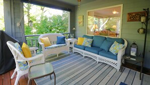 A covered porch with wicker furniture, a blue sofa, and a ceiling fan.