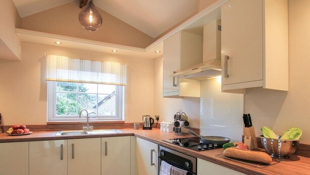 A modern kitchen with white cabinets, a wooden countertop, a built-in oven, and a window with curtains. - Little Bakehouse (Criccieth)