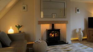 A cozy living room with a fireplace, a sofa, a knitted pouf, and a large vase. - Little Bakehouse (Criccieth)