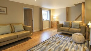 A spacious living room with two leather sofas, a patterned rug, and a wooden floor. - Little Bakehouse (Criccieth)