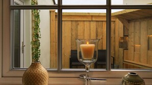 A window with a candle in a glass holder, a decorative vase, and a potted plant. - Little Bakehouse (Criccieth)
