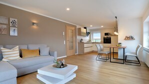 A modern apartment with a grey sofa, a white coffee table, a kitchen with a microwave, and a dining area with a table and chairs. - Vacation apartment I Kleine - Eifel - Time out (Hambuch)
