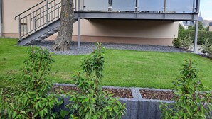A building with a staircase leading to a balcony, surrounded by a well-maintained lawn and small shrubs. - Vacation apartment I Kleine - Eifel - Time out (Hambuch)