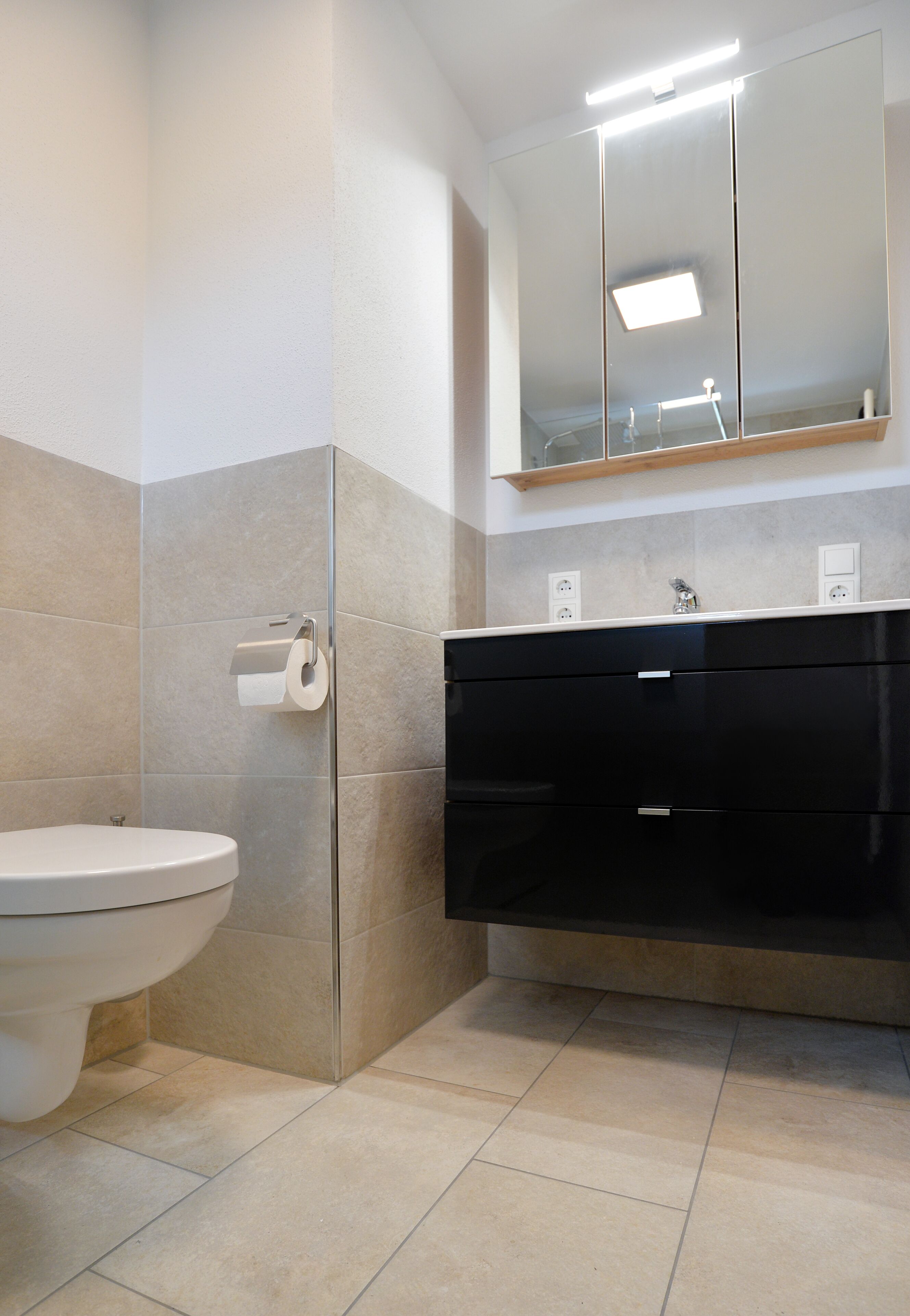 Une salle de bain avec des toilettes, un miroir et un meuble-lavabo noir.